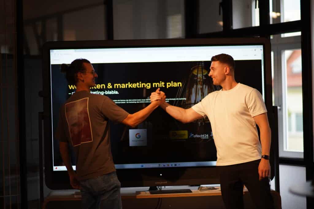 Die Gründer von wiwamedia geben sich vor einem Bildschirm mit dem Slogan Webseiten und Marketing mit Plan die Hand